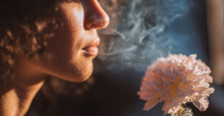 A young woman gently inhales the scent of fresh sage leaves with closed eyes, illustrating the deep emotional connection between aroma and memory.